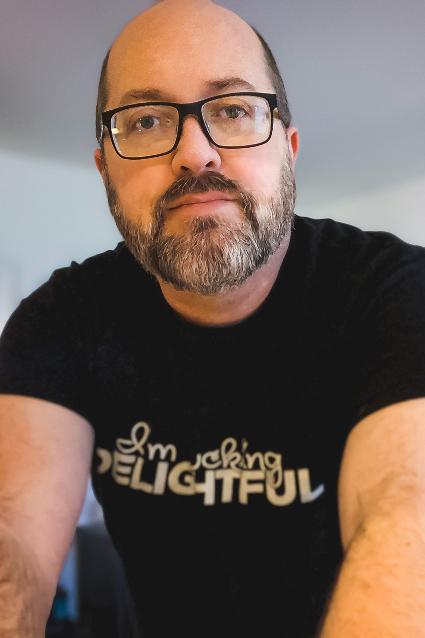 Bearded person in glasses and black t-shirt with text that says 'I'm Fucking Delightful'