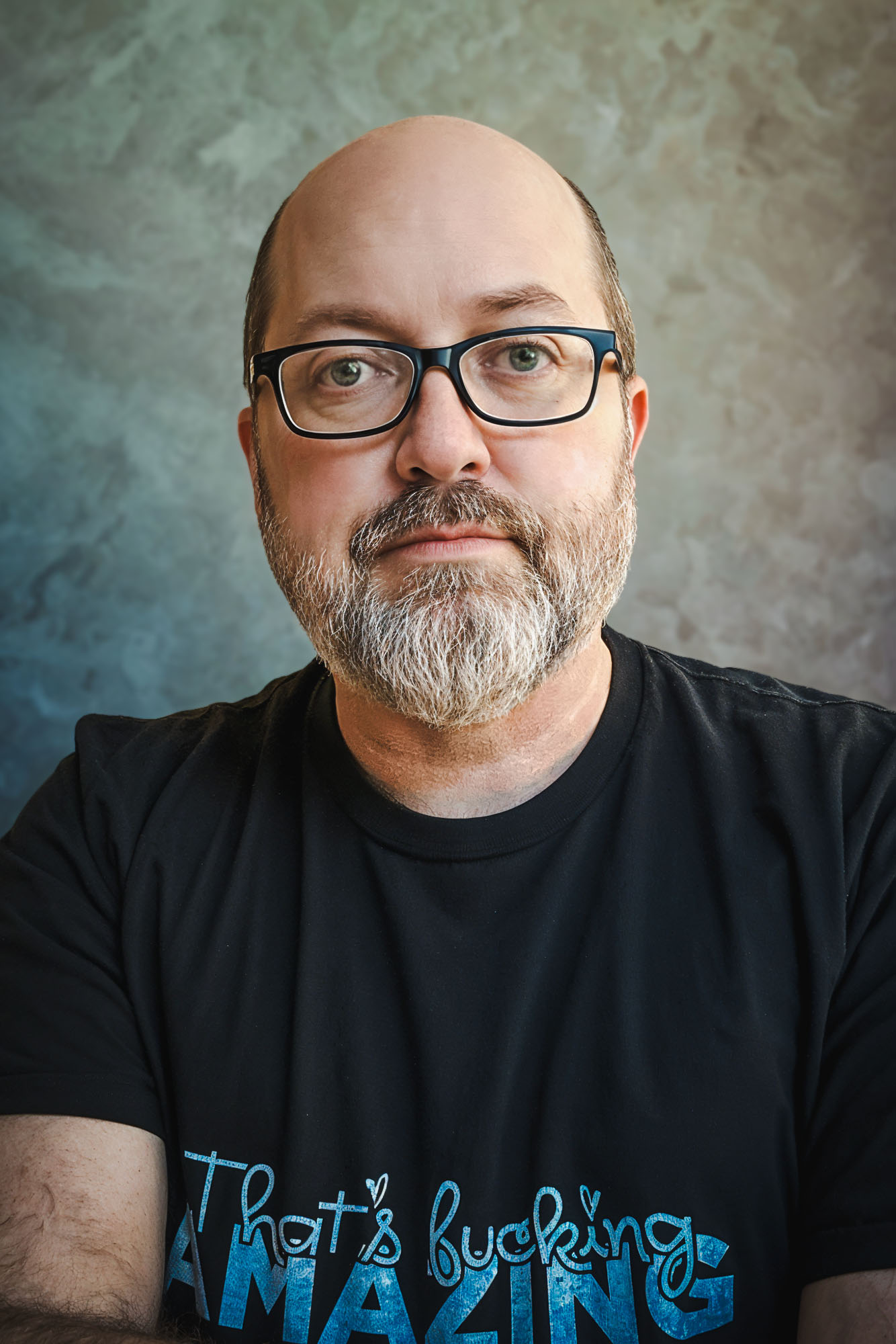 Balding, bearded person in glasses and black t-shirt